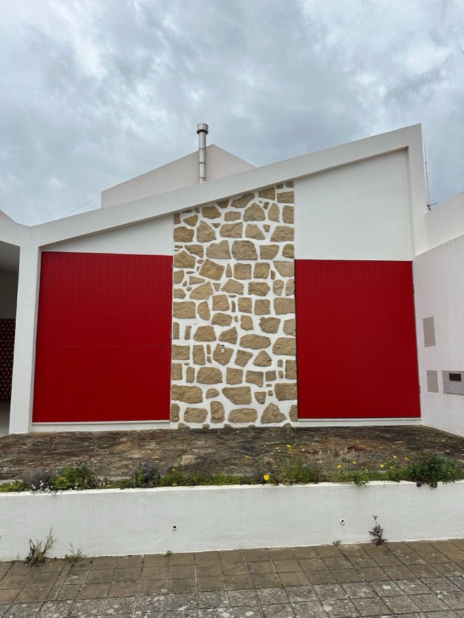 Portões lacados a vermelho encastrados numa parede de pedra